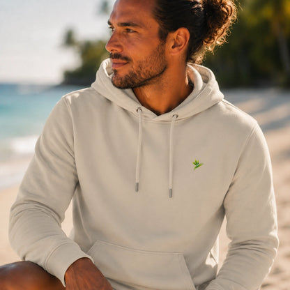 Homme de face portant le hoodie Signature beige en coton bio de la marque Viror, avec une illustration botanique de Rhaphidophora Tetrasperma Variegata sur fond de plage tropicale
